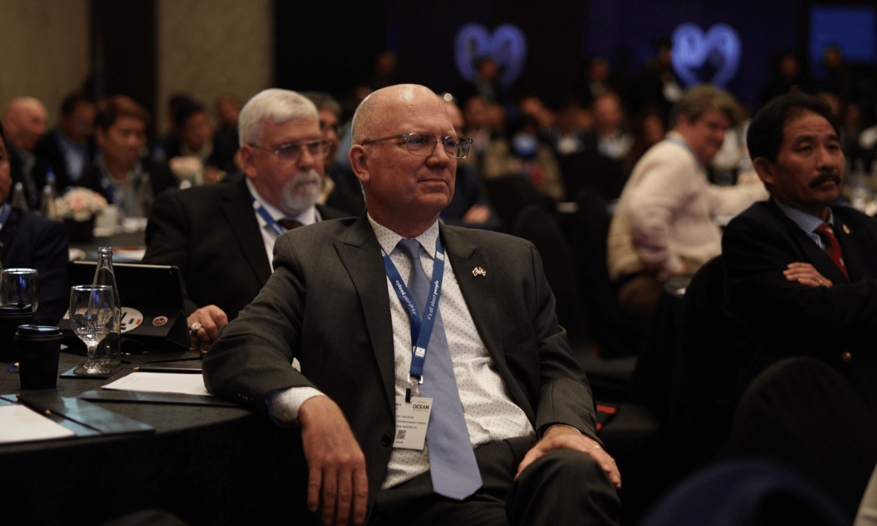 A man in a business suit sits in the conference, listening intently
